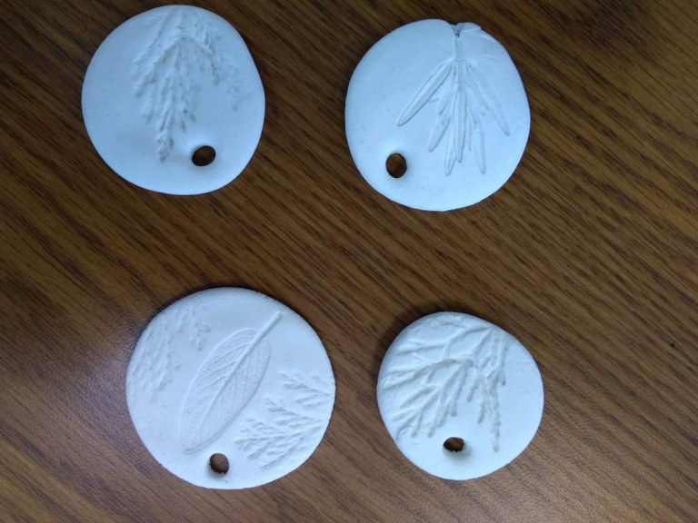 A photograph of four white circular pendants, each with an impression of a leaf on them.