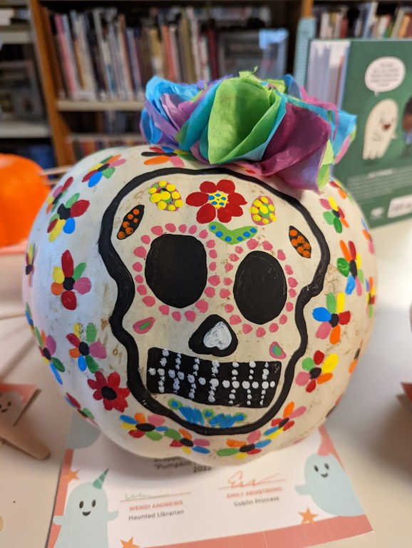 A photo of a round white gourd that has had a skull and flowers painted on it in the style of Mexican sugar skulls.