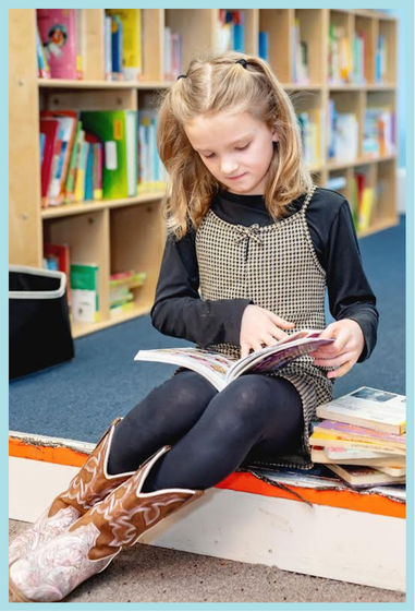 A photograph of a child reading a book in the library.