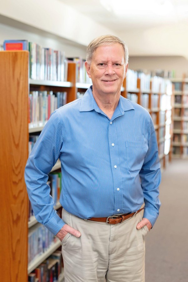 A photograph of Jeff Weiss in front of bookshelves.
